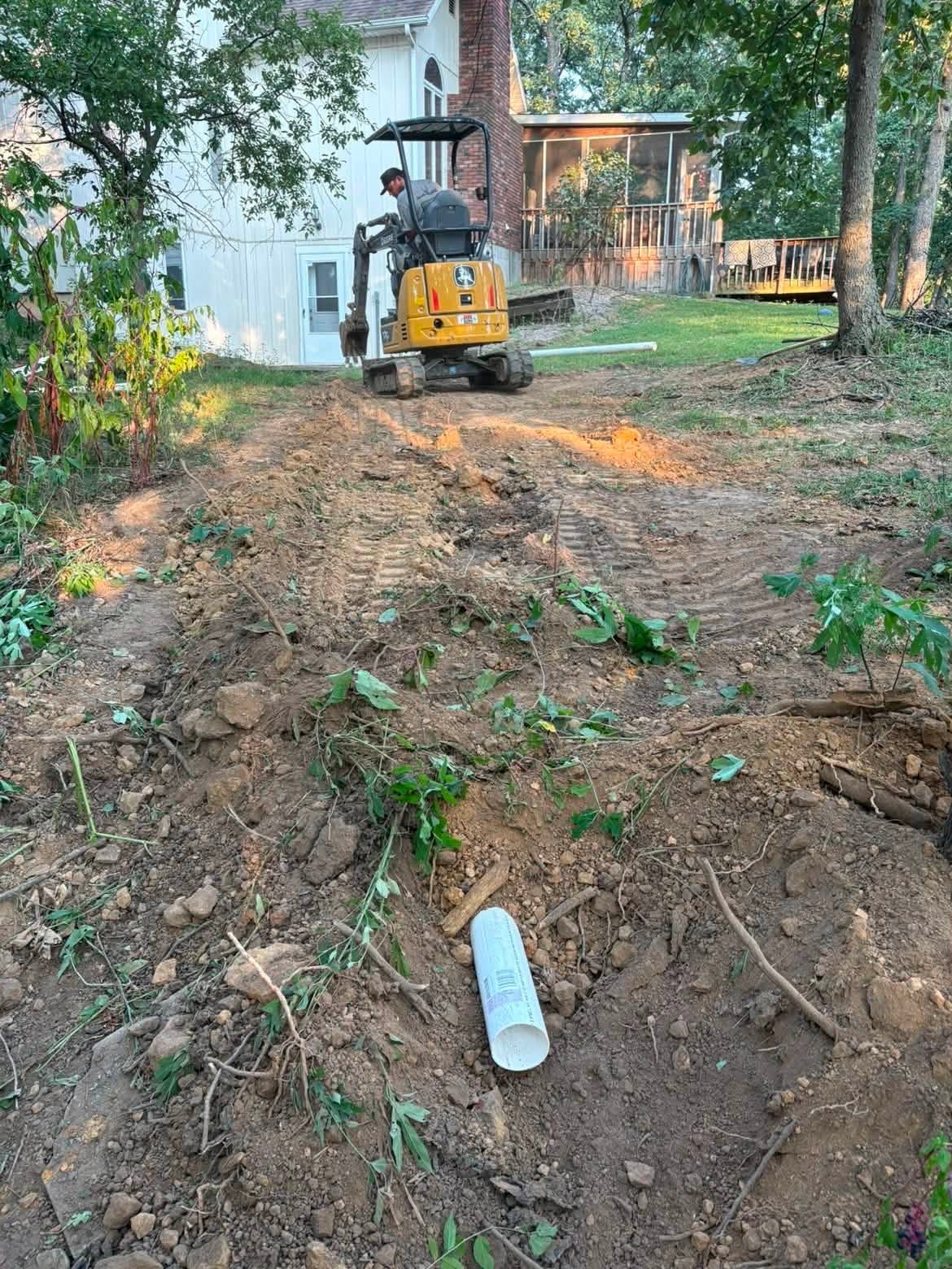 Mini excavator laying PVC pipe during sewer work in Vernon County, MO